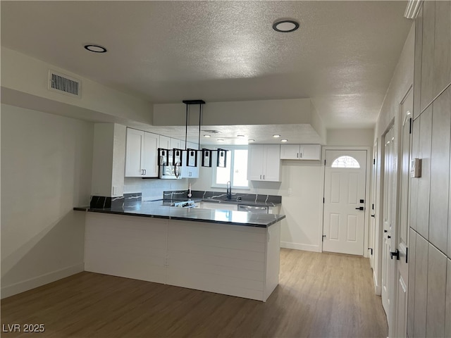 kitchen featuring decorative light fixtures, dishwasher, white cabinets, light hardwood / wood-style floors, and kitchen peninsula