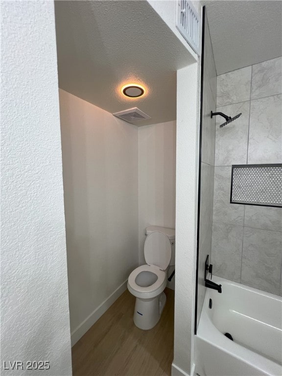 bathroom featuring tiled shower / bath, toilet, hardwood / wood-style floors, and a textured ceiling