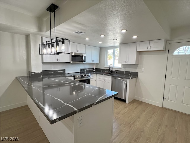 kitchen with appliances with stainless steel finishes, pendant lighting, white cabinetry, kitchen peninsula, and light wood-type flooring