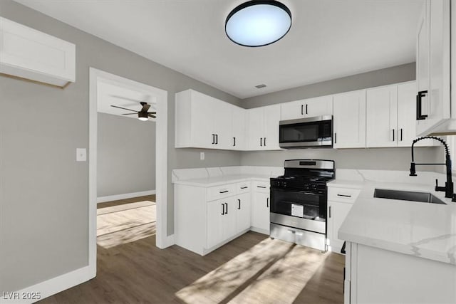 kitchen with appliances with stainless steel finishes, dark hardwood / wood-style floors, white cabinetry, sink, and light stone countertops