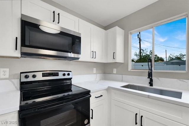 kitchen with electric stove, sink, white cabinetry, and light stone counters