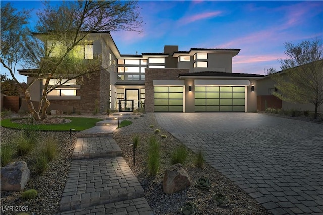 contemporary house with a garage, stone siding, decorative driveway, and stucco siding