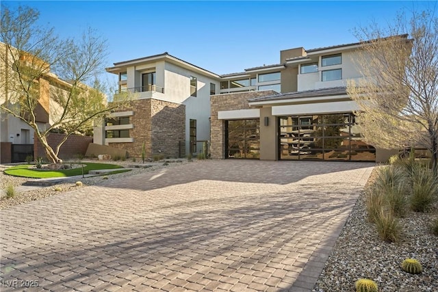 prairie-style home with decorative driveway, stone siding, an attached garage, and stucco siding