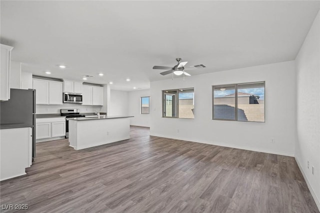 kitchen with white cabinetry, appliances with stainless steel finishes, an island with sink, and wood-type flooring