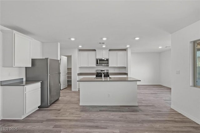 kitchen with light hardwood / wood-style floors, stainless steel appliances, an island with sink, and white cabinets