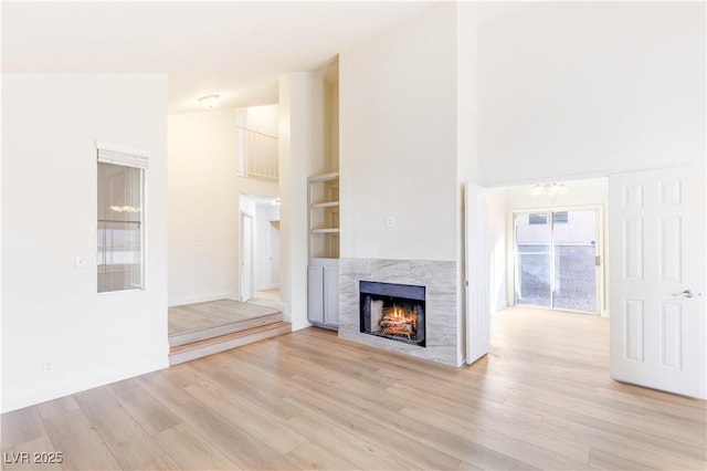 unfurnished living room with built in shelves, high vaulted ceiling, a premium fireplace, and light wood-type flooring