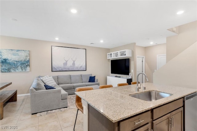 kitchen featuring light stone counters, sink, stainless steel dishwasher, and an island with sink