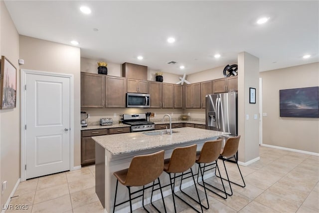 kitchen featuring sink, a breakfast bar area, light stone counters, stainless steel appliances, and a kitchen island with sink