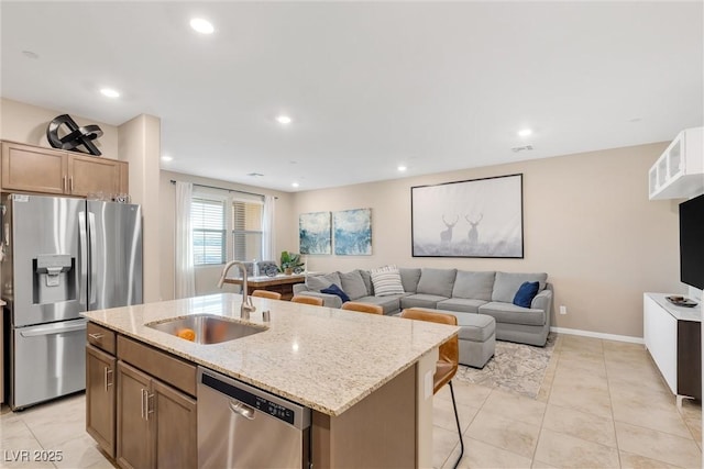 kitchen with sink, a breakfast bar, appliances with stainless steel finishes, light stone countertops, and a center island with sink