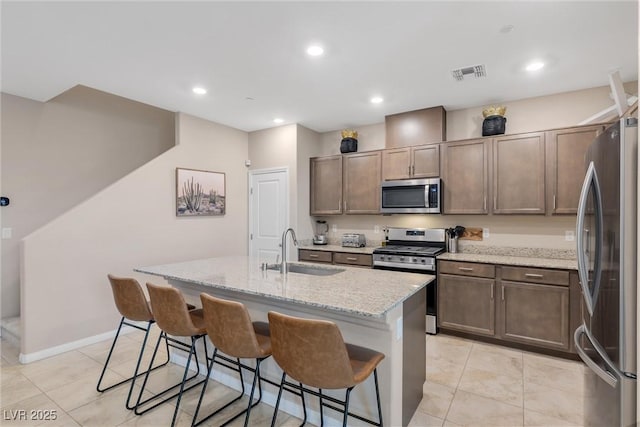 kitchen featuring light stone counters, appliances with stainless steel finishes, sink, and a kitchen island with sink