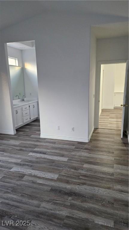 unfurnished bedroom featuring a sink, ensuite bathroom, baseboards, and dark wood-style flooring