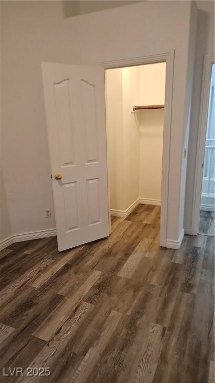 unfurnished bedroom featuring a walk in closet, dark wood-style floors, and baseboards