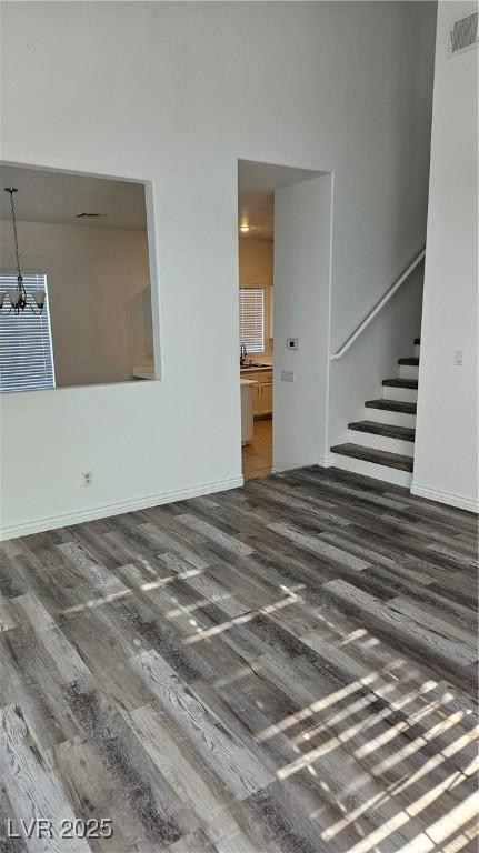 unfurnished living room featuring stairway, dark wood-style floors, visible vents, baseboards, and an inviting chandelier