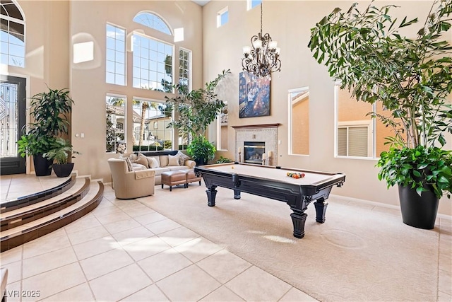 game room with a high ceiling, a tile fireplace, a wealth of natural light, and light carpet