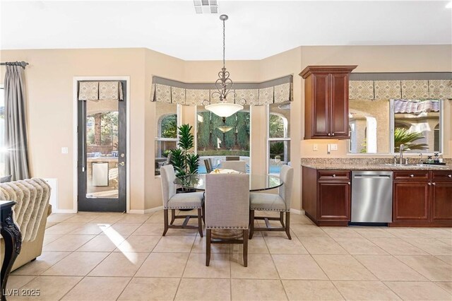 kitchen featuring light tile patterned flooring, sink, light stone counters, decorative light fixtures, and stainless steel dishwasher