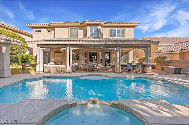 rear view of property featuring an outdoor living space, a pool with connected hot tub, stucco siding, a patio area, and outdoor dry bar