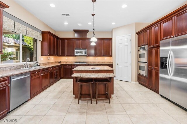 kitchen featuring sink, light tile patterned floors, appliances with stainless steel finishes, a kitchen island, and pendant lighting