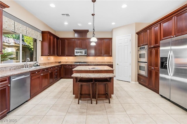 kitchen featuring visible vents, a center island, light stone countertops, stainless steel appliances, and a sink