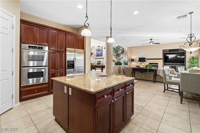 kitchen featuring light tile patterned flooring, a kitchen island, decorative light fixtures, stainless steel appliances, and light stone countertops