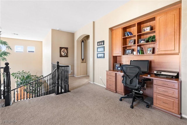 office featuring baseboards, arched walkways, and light carpet