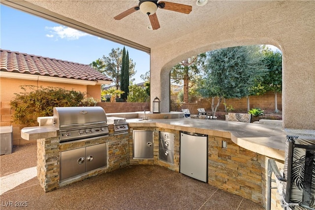 view of patio / terrace featuring grilling area, a fenced backyard, a ceiling fan, and exterior kitchen