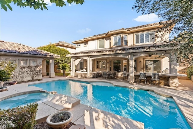 back of house featuring stucco siding, a tile roof, a pool with connected hot tub, an outdoor hangout area, and a patio area