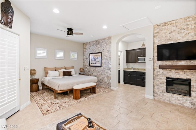 bedroom with connected bathroom, a stone fireplace, and ceiling fan