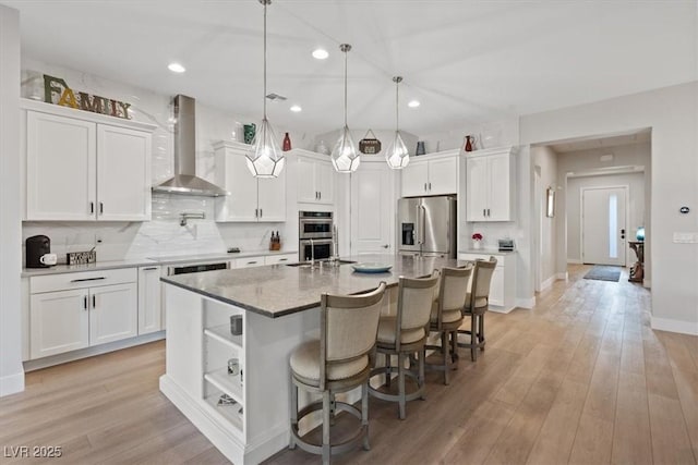 kitchen featuring stainless steel appliances, a kitchen island with sink, wall chimney range hood, and white cabinets