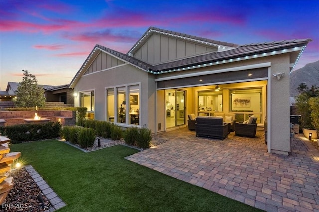 back house at dusk with a yard, an outdoor living space with a fire pit, and a patio area