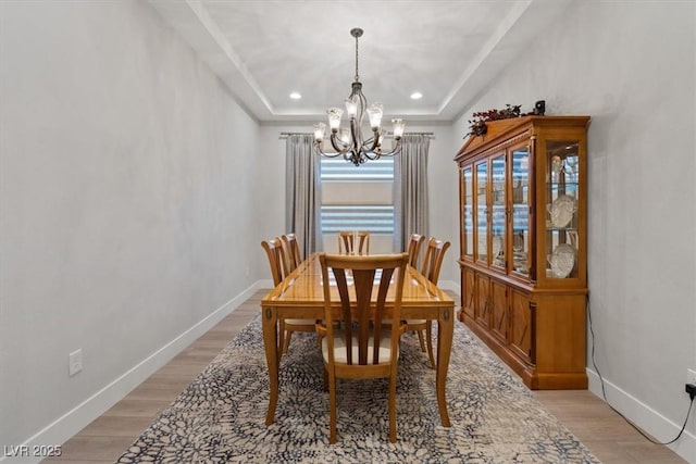 dining space with an inviting chandelier, a tray ceiling, and light wood-type flooring