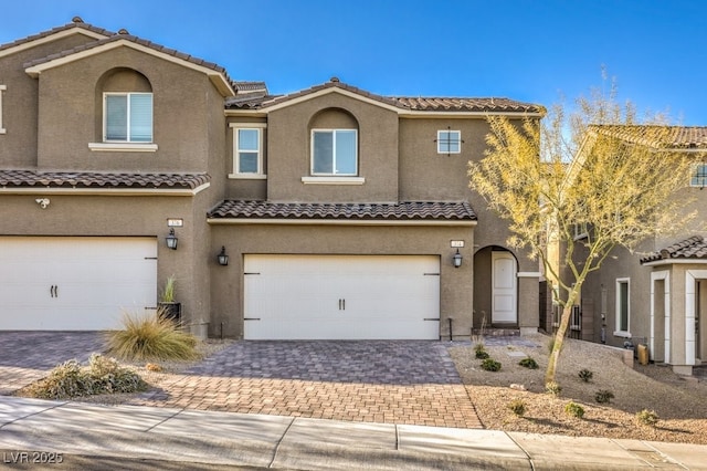 townhome / multi-family property with a garage, decorative driveway, and stucco siding