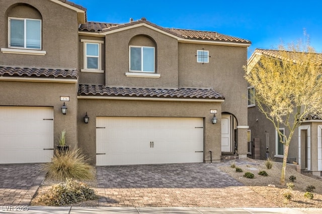 multi unit property featuring a garage, decorative driveway, a tile roof, and stucco siding