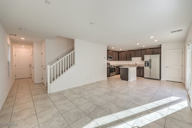 kitchen with dark brown cabinetry, a kitchen island, light tile patterned flooring, and appliances with stainless steel finishes