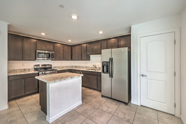 kitchen featuring dark brown cabinetry, sink, a center island, appliances with stainless steel finishes, and light stone countertops