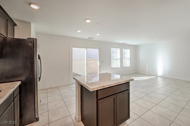 kitchen with dark brown cabinetry, a center island, light stone counters, and stainless steel refrigerator