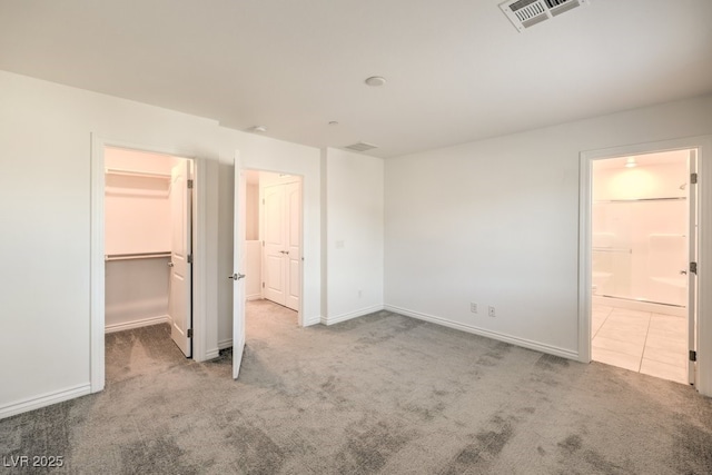 unfurnished bedroom with ensuite bathroom, a spacious closet, and light carpet