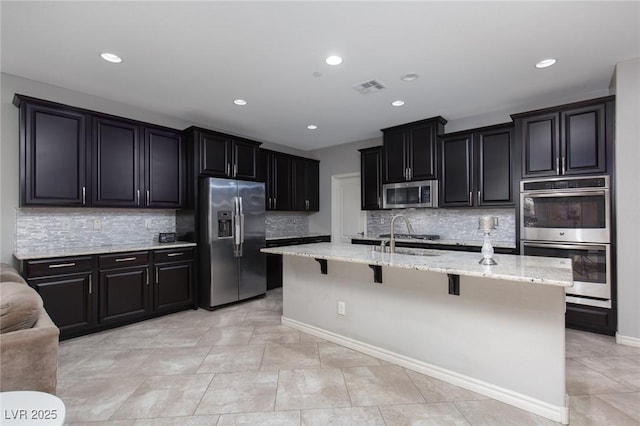 kitchen featuring a breakfast bar, visible vents, appliances with stainless steel finishes, a sink, and light stone countertops