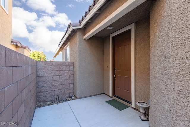 property entrance with fence, a patio, and stucco siding