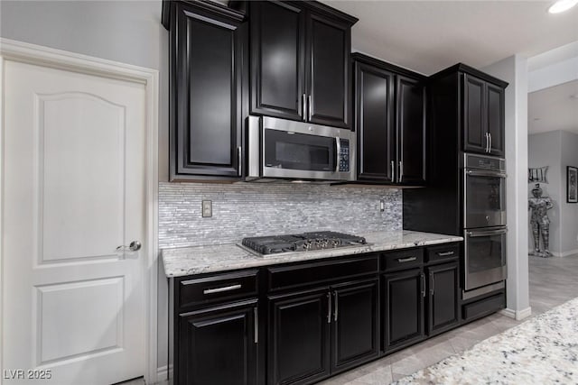 kitchen featuring stainless steel appliances, dark cabinetry, and backsplash