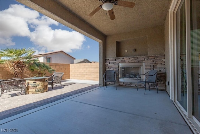 view of patio featuring a ceiling fan, an outdoor stone fireplace, and fence