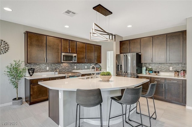 kitchen featuring dark brown cabinetry, sink, decorative light fixtures, an island with sink, and stainless steel appliances