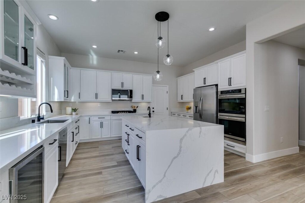 kitchen with appliances with stainless steel finishes, white cabinetry, sink, wine cooler, and a center island