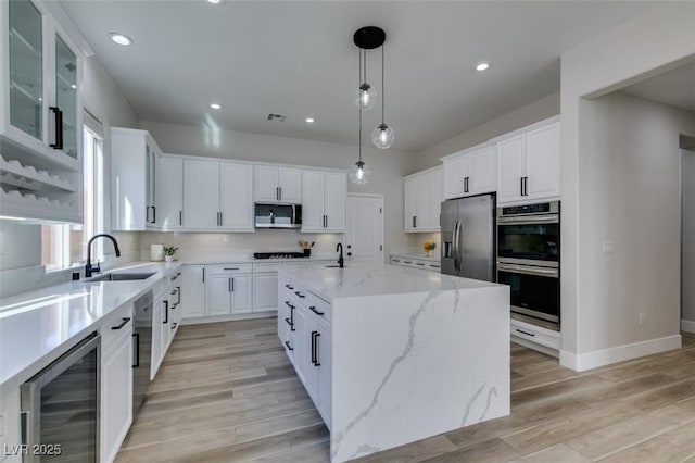 kitchen with appliances with stainless steel finishes, white cabinetry, sink, wine cooler, and a center island