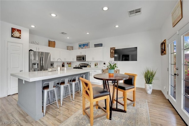 kitchen with light hardwood / wood-style flooring, a breakfast bar area, stainless steel appliances, white cabinets, and a center island with sink