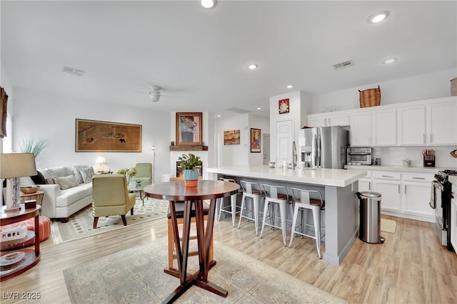 kitchen with a breakfast bar, stainless steel fridge with ice dispenser, light hardwood / wood-style flooring, a kitchen island with sink, and white cabinets