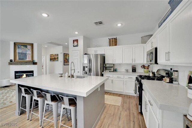 kitchen featuring sink, white cabinetry, a center island with sink, appliances with stainless steel finishes, and a kitchen breakfast bar