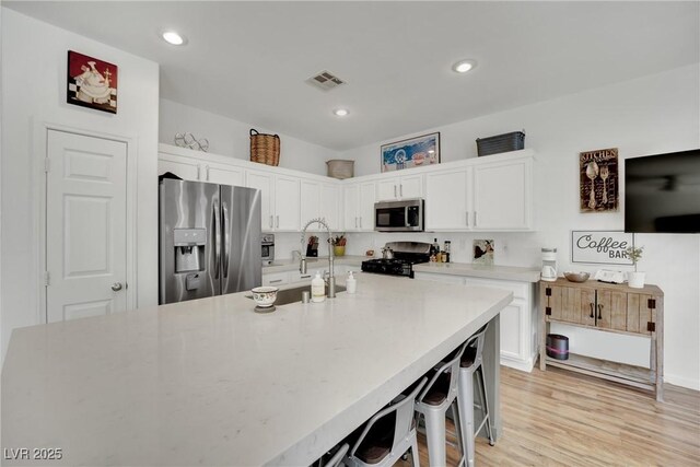 kitchen with appliances with stainless steel finishes, a breakfast bar, light wood-type flooring, and white cabinets