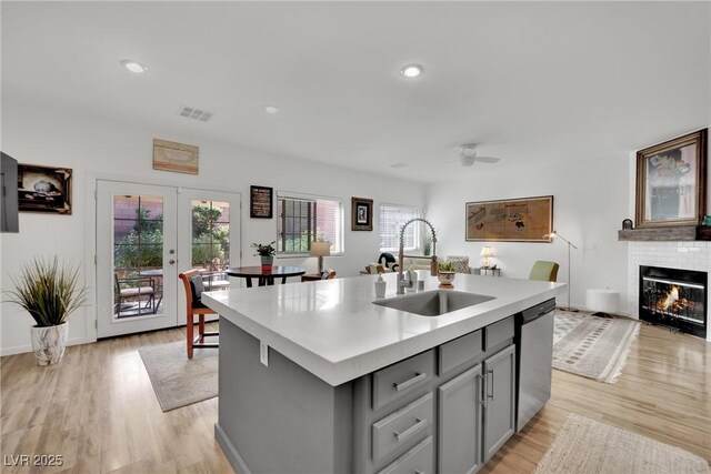 kitchen featuring gray cabinets, dishwasher, sink, a center island with sink, and light hardwood / wood-style flooring