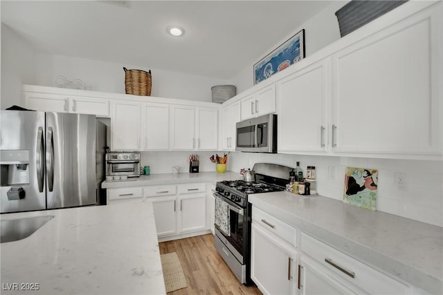 kitchen featuring appliances with stainless steel finishes, light stone counters, white cabinets, and light wood-type flooring