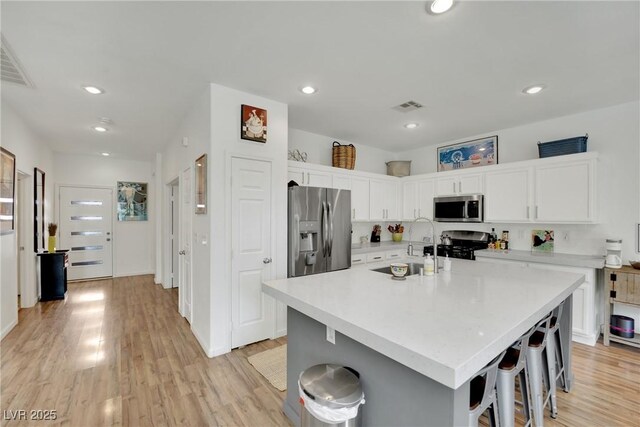 kitchen featuring an island with sink, white cabinetry, a kitchen bar, stainless steel appliances, and light wood-type flooring